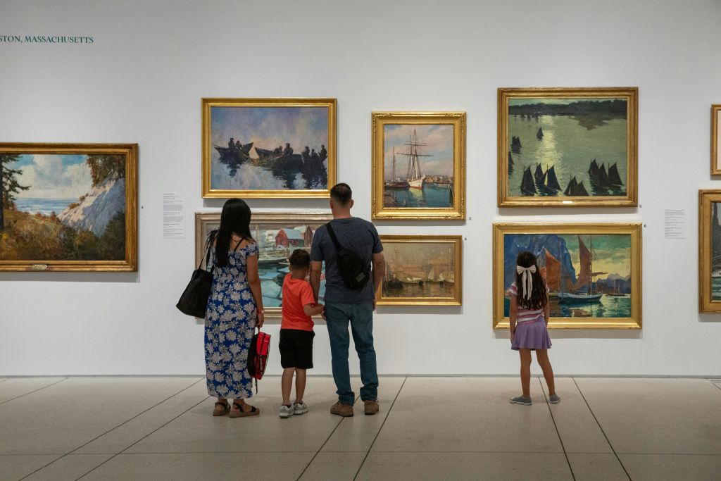 미술관에 서 있는 4인 가족이 하얀 벽에 그려진 해양 및 해양 장면의 그림을 관찰하고 있습니다.