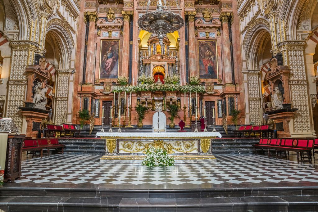 황금색 디테일의 화려한 교회 제단, 꽃 장식, 종교 회화, 체크무늬 바닥이 웅장한 배경을 배경으로 합니다.