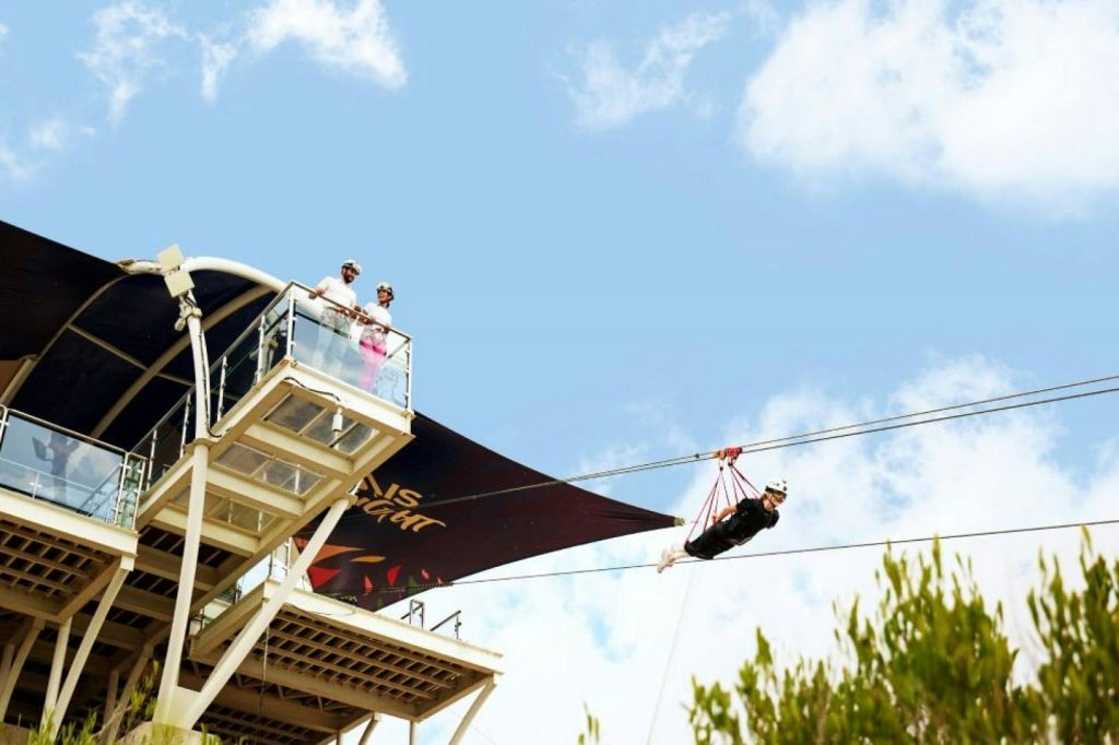 구름과 초록이 깔린 푸른 하늘을 배경으로 관람객이 지켜보는 가운데 플랫폼에서 집업을 하고 있는 사람.