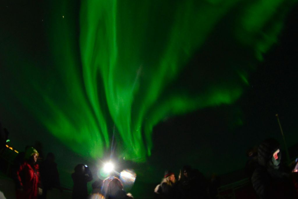 북극광 아래에서 크루즈를 즐기는 승객들은 초록빛 하늘 아래에서 사진을 찍습니다.