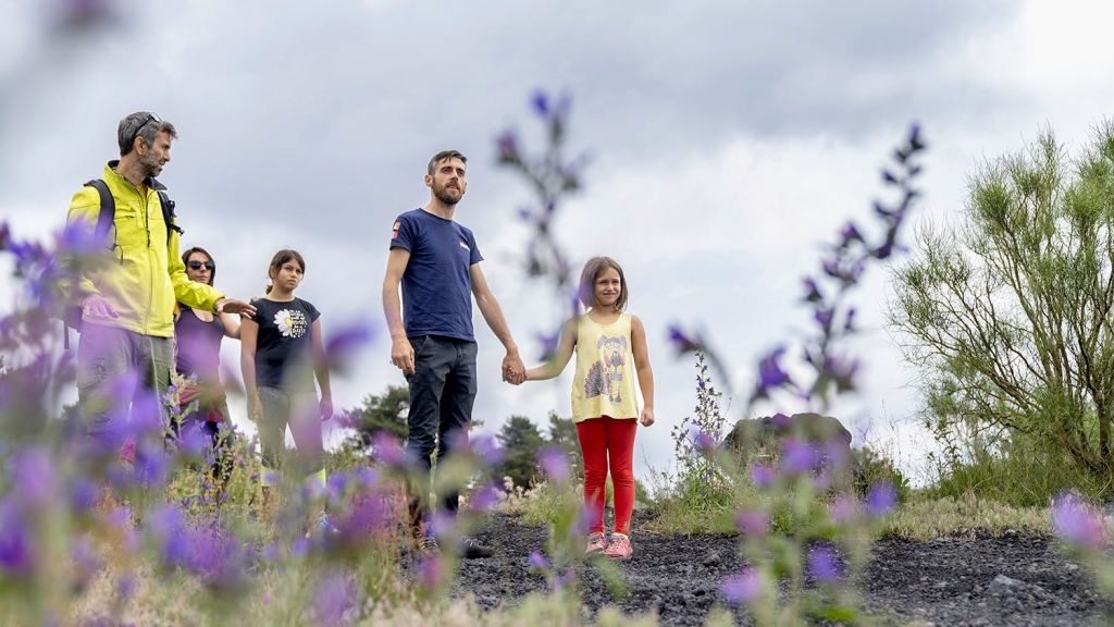 노란 재킷을 입은 남성과 두 아이를 포함한 다른 세 명이 흐린 하늘 아래 보라색 꽃밭에 서 있습니다.