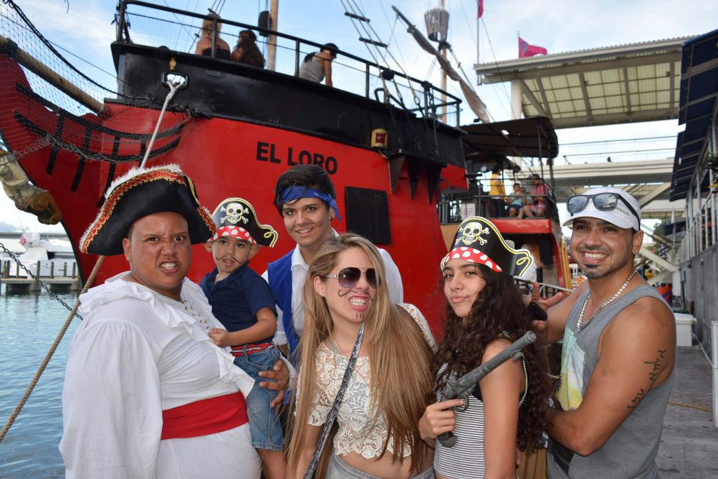 '엘 로로' 라는 이름의 붉은 배 앞에서 웃으며 포즈를 취하는 해적 의상을 입은 사람들이 바닷가에 정박했습니다.