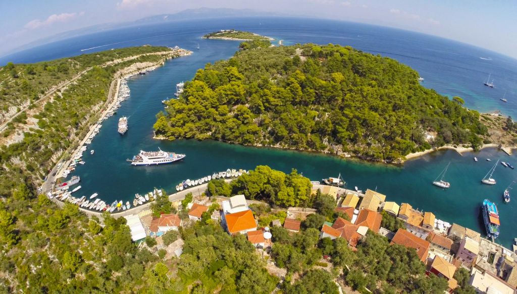 붉은 지붕의 집, 울창한 숲이 우거진 반도, 강 위의 보트, 푸른 바다를 둘러싼 해안 마을의 공중 전망.