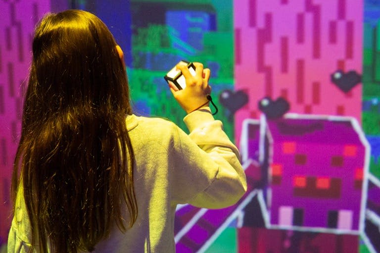 작은 기기를 들고 있는 사람은 대화형 전시물에서 다채로운 픽셀화 디지털 디스플레이를 마주할 수 있습니다.