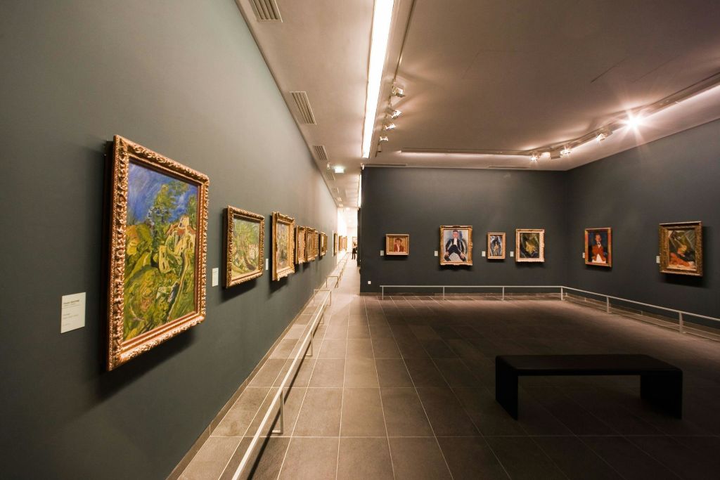 벽에 액자 그림, 전경에 벤치, 머리 위 조명이 있는 아트 갤러리 내부.