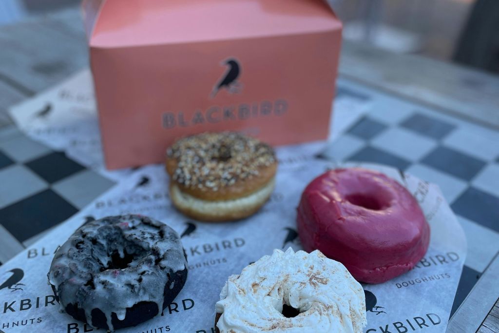 블랙버드 로고가 새겨진 분홍색 상자 앞에 있는 블랙버드 상표가 새겨진 종이에 네 가지 도넛을 놓아주세요.
