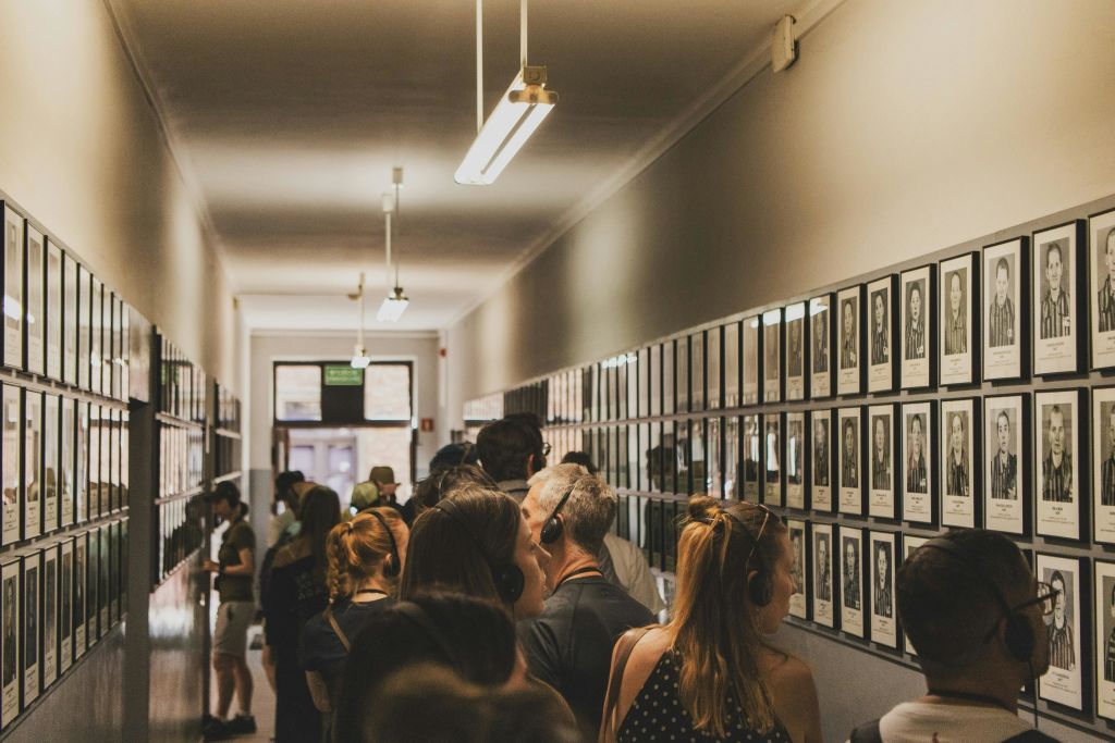 밝은 조명 아래에서 많은 사람들이 헤드폰을 착용하고 있는, 액자에 담긴 사진 벽을 보고 있는 복도의 사람들.