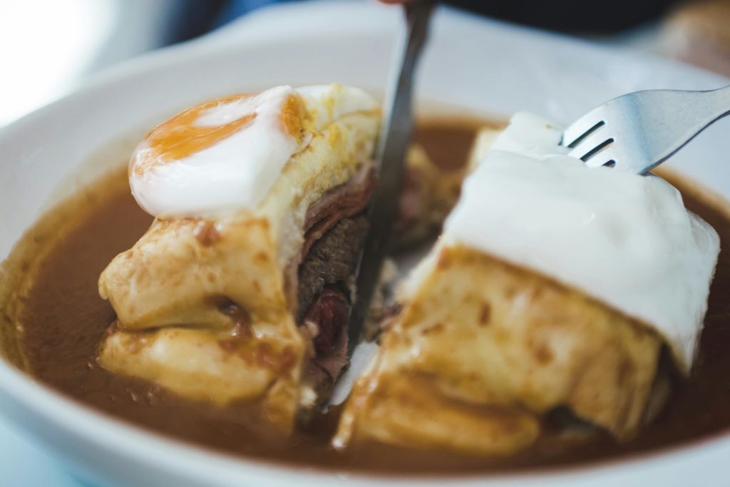 하얀 접시에 고기, 치즈, 달걀, 소스를 층층이 쌓아 샌드위치를 자른 사람의 클로즈업.