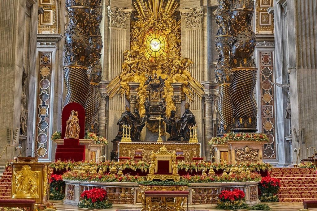 황금색 디테일, 레드 벨벳 시트, 꽃 장식, 조각상이 돋보이는 화려한 제단 위에 빛나는 조명이 비춰진 센터피스가 장식되어 있습니다.