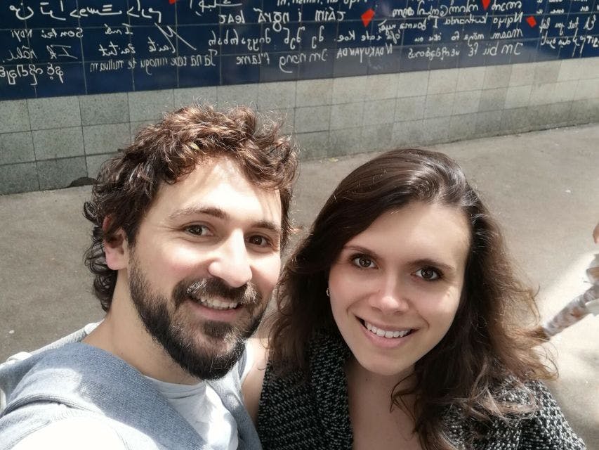 다양한 대본과 방정식으로 뒤덮인 벽을 배경으로 카메라를 바라보며 웃고 있는 남녀.