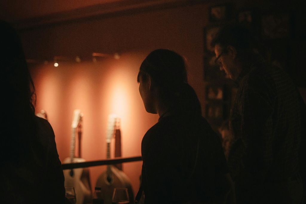 어쿠스틱 기타가 배경에 따뜻하게 빛나는 벽을 배경으로 어쿠스틱 기타가 어우러진 어두운 방에서 사람들이 뒤에서 바라보았다.