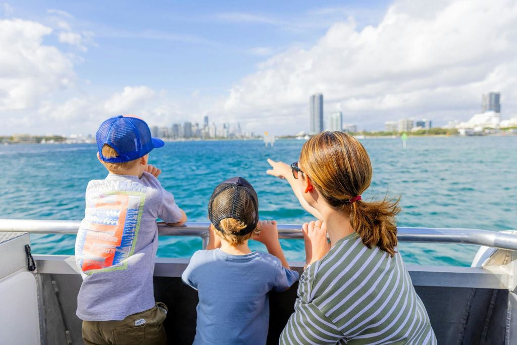 화창한 날 물 건너편에 있는 도시의 스카이라인을 바라보는 세 명의 사람이 보트를 타고 있습니다.