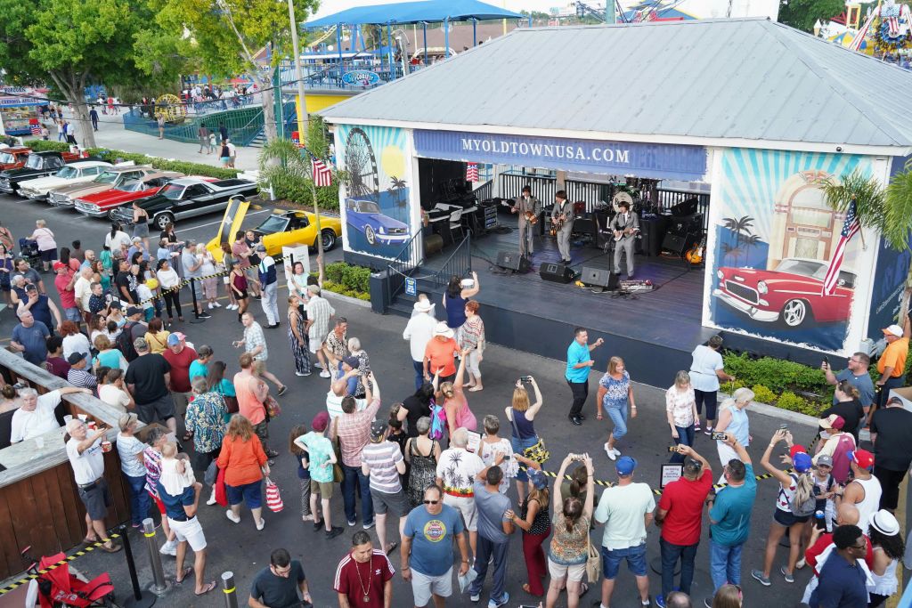 이벤트 공간에서 클래식 자동차 옆 야외 무대에서 밴드의 라이브 음악을 즐기고 있습니다.