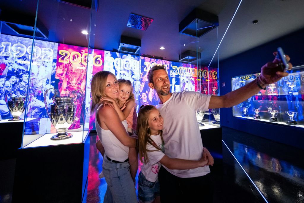 가족이 스포츠 트로피와 화려한 조명을 배경으로 박물관에서 셀카를 찍고 있습니다.