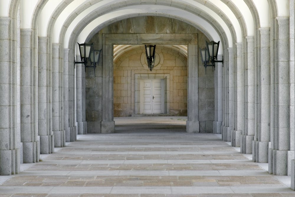 등불이 있는 석조 아치형 통로는 건물 내부에 또 다른 아치형 통로가 있는 흰색 이중문으로 이어집니다.