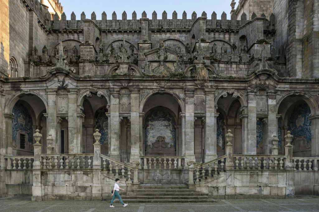한 사람이 아치형 출입구와 섬세한 건축 조각이 있는 화려하고 오래된 석조 건물 앞을 걸어가고 있습니다.