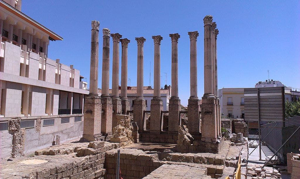 현대적인 건물 사이에 위치한 맑고 푸른 하늘을 배경으로 부분적으로 복원된 화려한 수도가 있는 8개의 고대 로마 기둥.