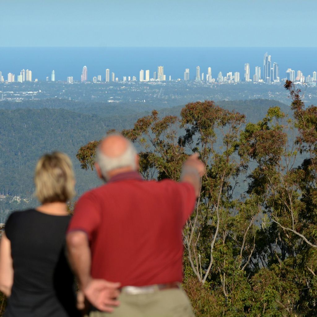 한 사람이 가리키고 있는 두 사람은 맑은 하늘 아래 숲 너머로 보이는 높은 건물이 있는 먼 도시의 스카이라인을 내려다보고 있습니다.