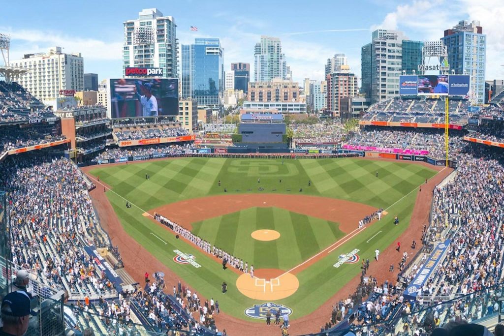 경기장에 선수들이 줄지어 서 있고 도시 스카이라인을 배경으로 관중들이 가득한 야구 경기장입니다.