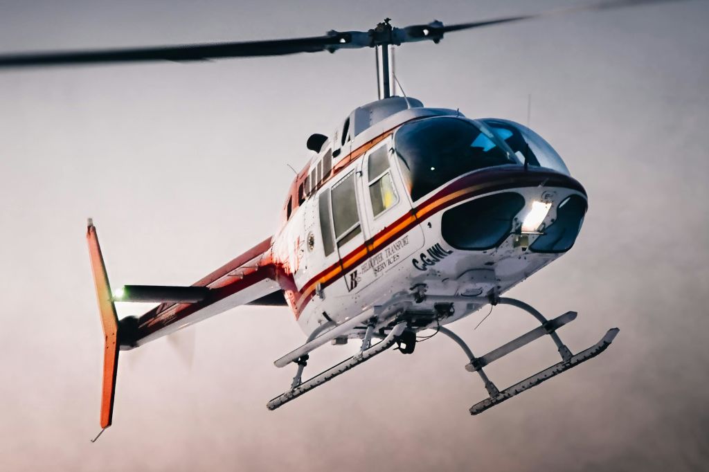 비행 중 흰색과 빨간색 헬리콥터가 눈에 띄는 착륙 스키드와 흐린 하늘을 향해 회전하는 블레이드를 갖추고 있습니다.