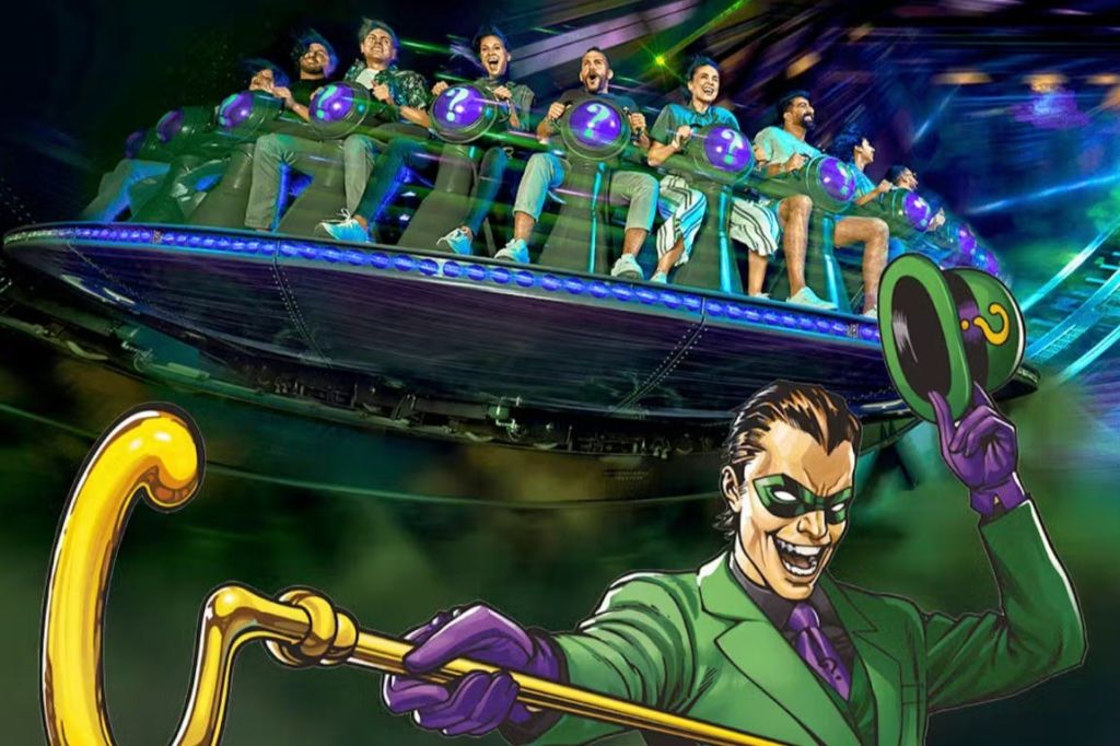 다채로운 Riddler 테마의 디자인으로 회전하는 놀이 기구에 앉아 밝은 불빛을 비추는 사람들.