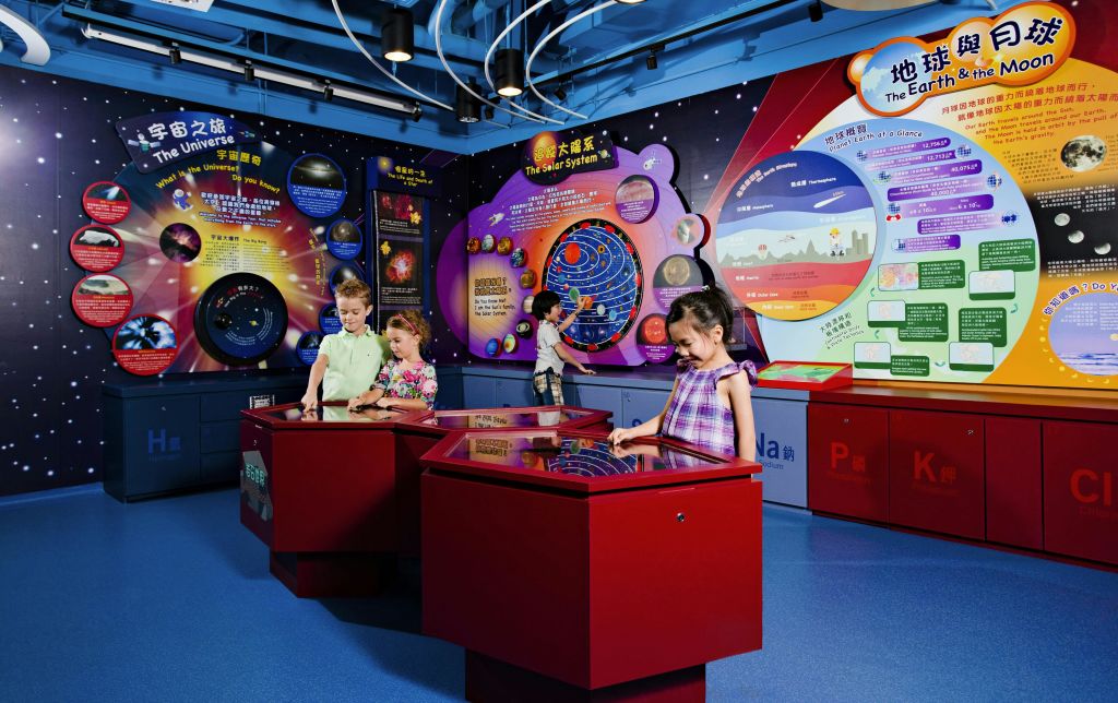 아이들은 우주와 태양계에 대한 포스터를 특징으로 하는 우주 테마 전시회에서 빨간색 터치스크린 디스플레이와 상호 작용합니다.