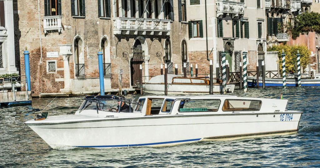 흰색 보트가 아치형 창문과 발코니가 있는 유서 깊은 건물 앞의 운하를 따라 움직입니다.