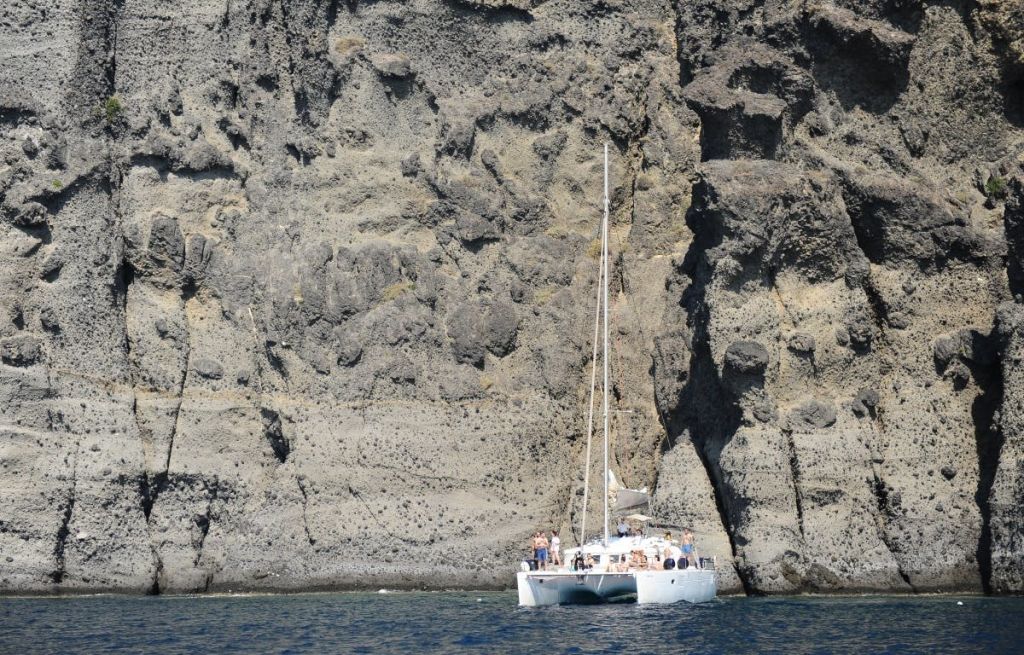 커다란 바위 절벽 얼굴 근처에 떠 있는 사람들이 탑승한 쌍동선.