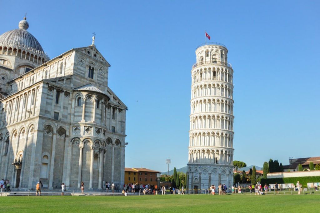 피사의 사탑과 햇살이 내리쬐는 마당에 있는 대성당으로, 방문객들은 산책을 하며 사진을 찍습니다.
