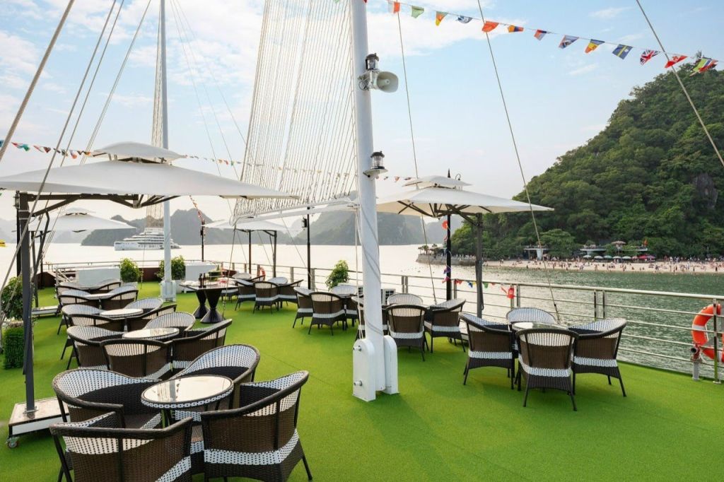 물과 언덕이 내려다보이는 녹색 인조 잔디에 테이블과 의자가 있는 야외 파티오, 우산과 줄 조명.