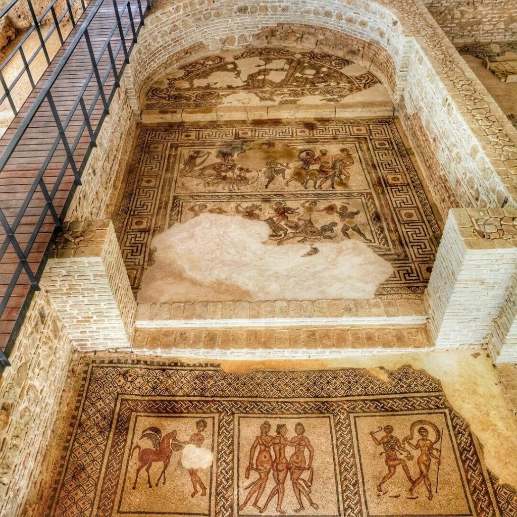 벽돌 벽과 금속 난간으로 둘러싸인 부분적으로 손상된 인간과 동물과의 장면을 묘사한 고대 로마의 모자이크.