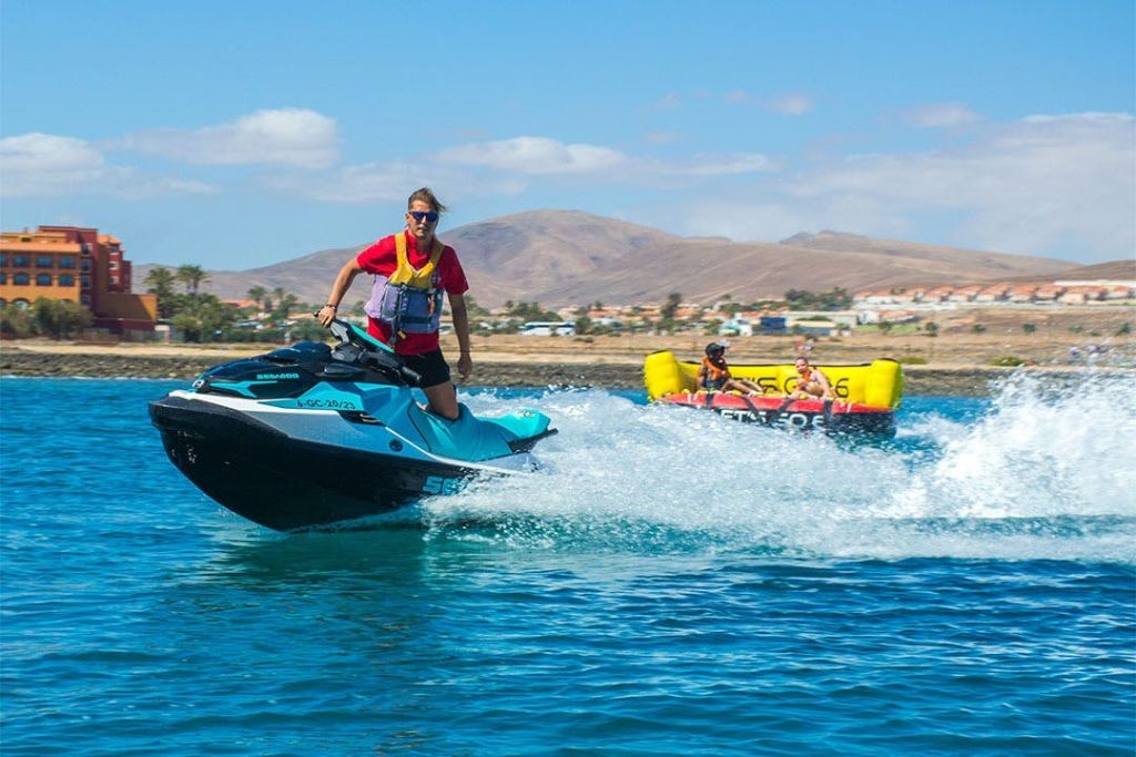 맑은 하늘 아래 건물과 언덕을 배경으로 해변 근처에서 제트 스키를 타는 사람.