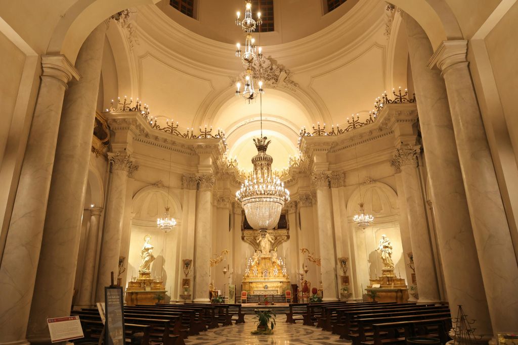 화려한 샹들리에, 조각상, 대리석 기둥, 따뜻한 조명으로 빛나는 정교한 제단이 있는 대성당 내부.