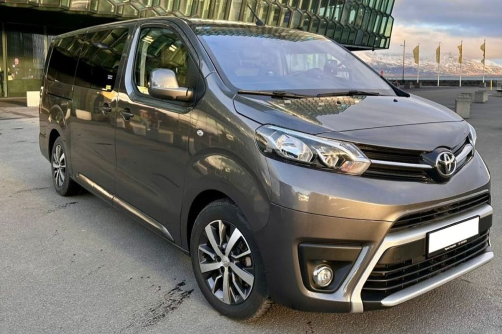 회색 미니밴이 현대적인 유리 정면 건물을 배경으로 거리에 주차되어 있습니다.