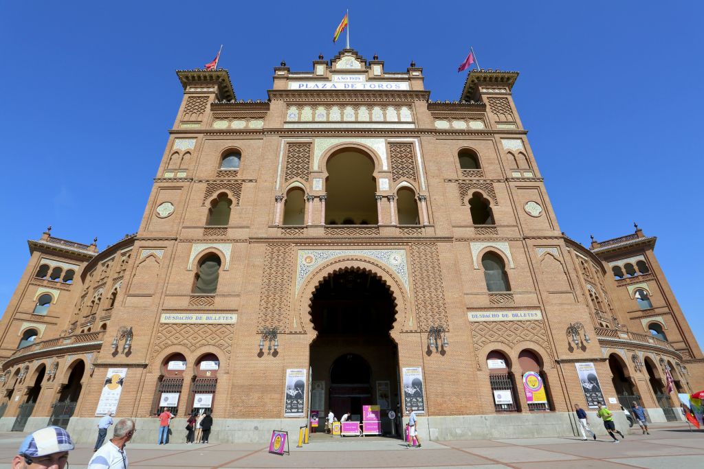 '토로스 광장' 이라고 표시된 아치형 입구가 있는 대형 벽돌 건물입니다. 화창한 날에는 여러 사람이 앞에 서 있습니다.