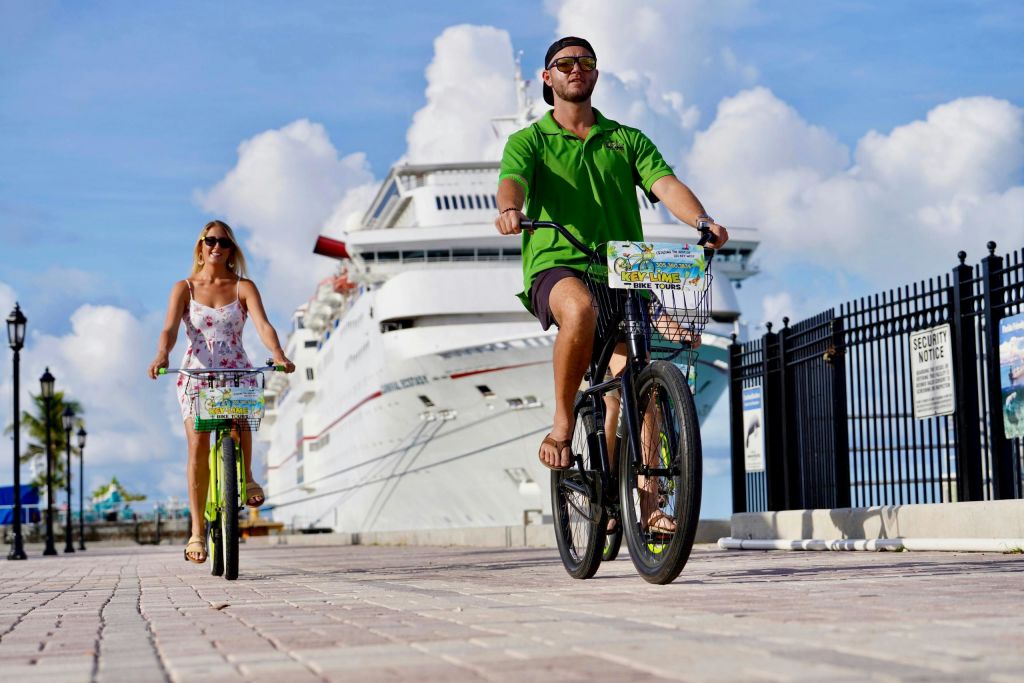 밝고 흐린 하늘 아래 도킹한 유람선 근처의 포장도로에서 자전거를 타고 있는 두 사람.