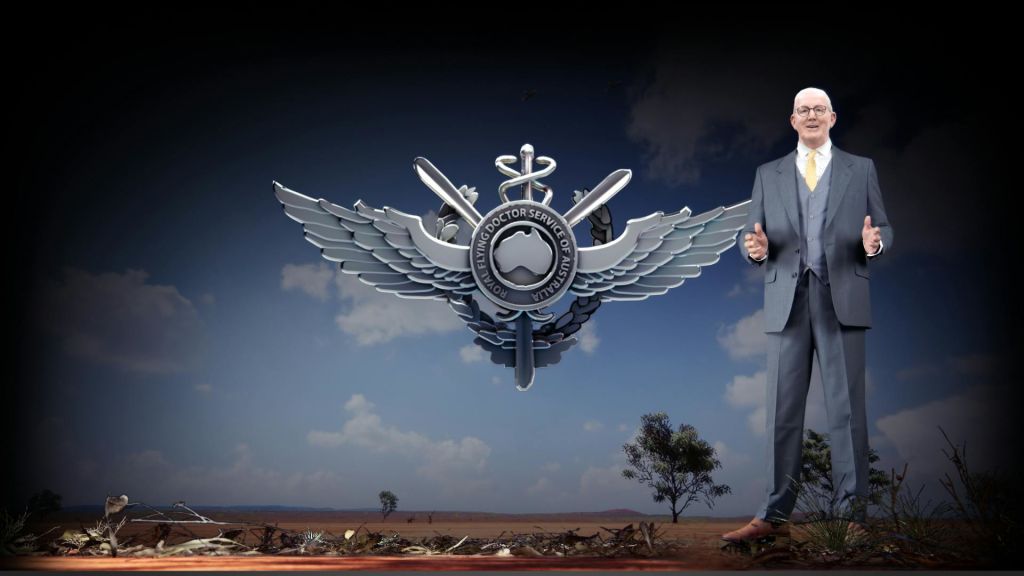 양복을 입은 노인이 Royal Flying Doctor Service 로고와 아웃백 풍경이 있는 배경 앞에 서 있습니다.