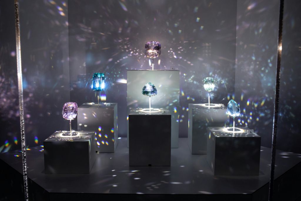 희미한 방의 흰색 받침대에 6개의 조명된 색상의 크리스탈이 표시되며 빛이 반사되어 반짝이는 효과를 만듭니다.