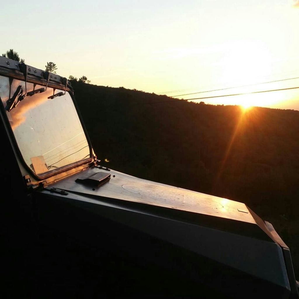 차량의 앞 유리창을 통해 바라보는 언덕 위 풍경의 석양.