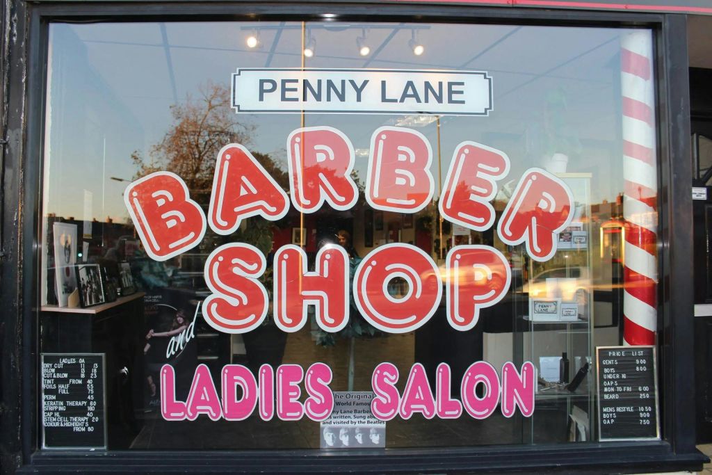 대담한 빨간색과 분홍색 글자로 된 "페니 레인 이발소 및 레이디스 살롱" 이 있는 상점 앞 창문.