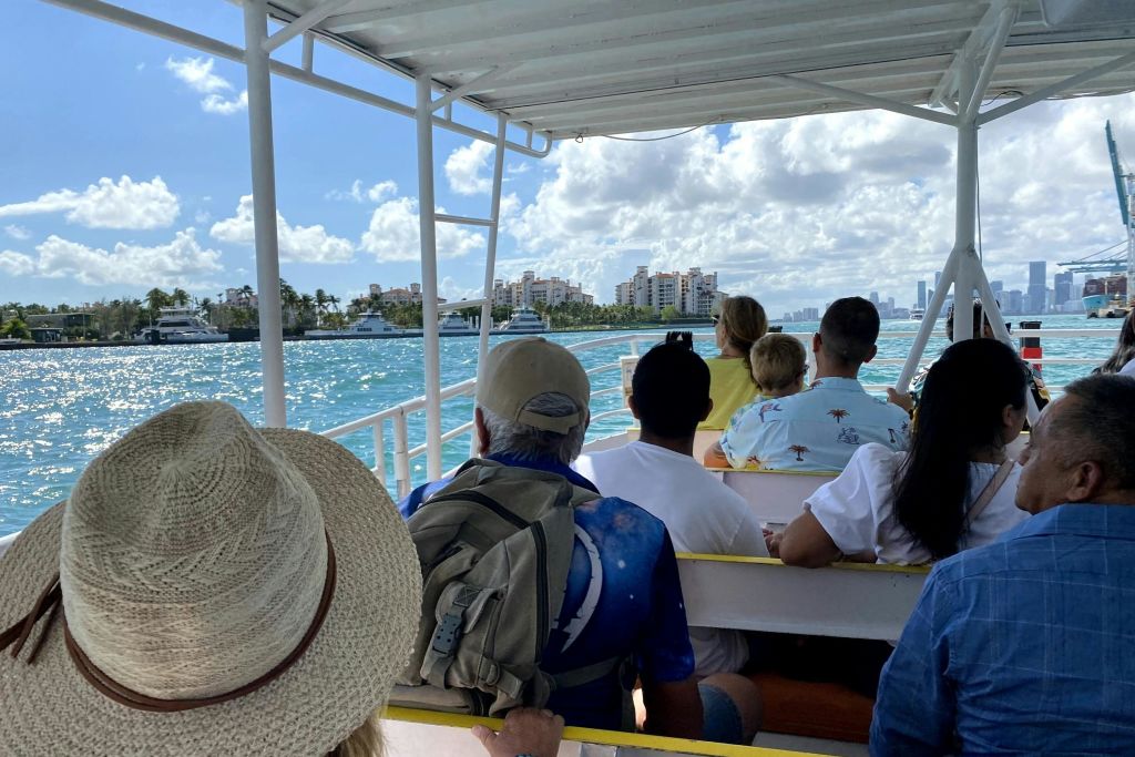 캐노피가 있는 보트에 앉아 흐린 하늘 아래 도시 풍경 근처의 푸른 물 위를 유람하는 사람들.