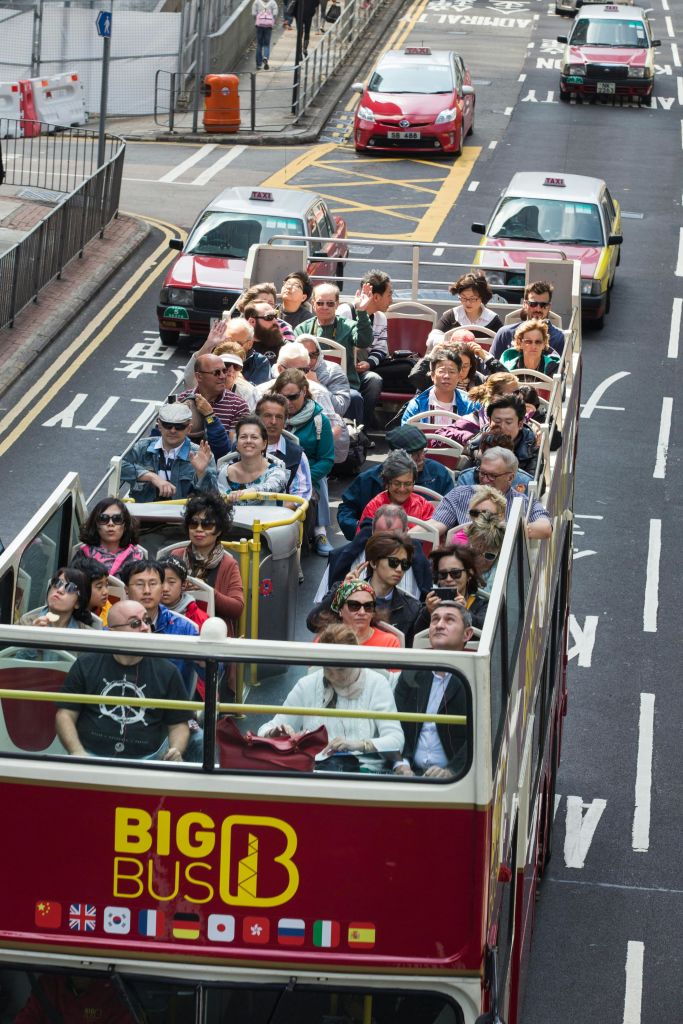 상층 갑판에 앉은 승객들로 가득한 2층 투어 버스가 택시가 있는 도시 거리를 운전하고 있습니다.