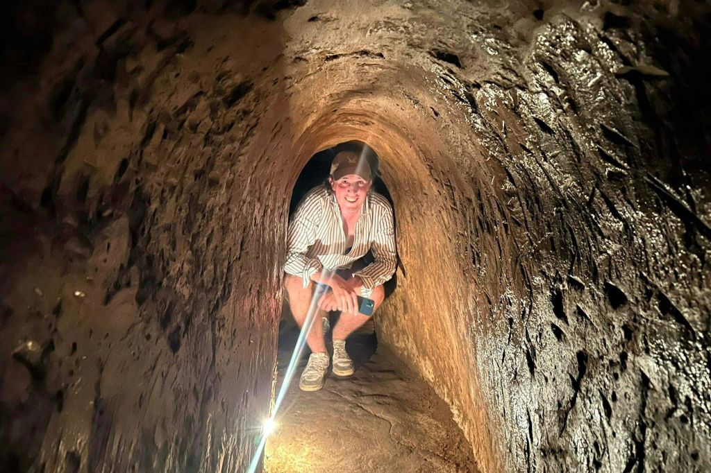 좁고 어두운 터널에 웅크리고 앉아 스마트폰을 들고 모자, 줄무늬 셔츠를 입은 사람.