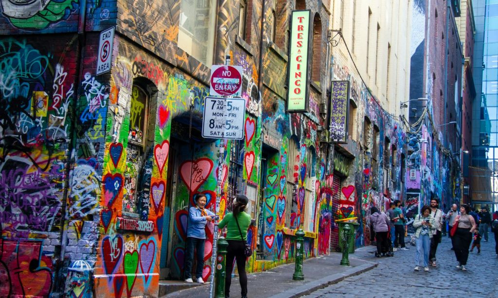 활기찬 심장 디자인이 돋보이는 그래피티로 덮인 골목에 서 있는 두 사람. 거리 표지판과 "Tres Acinco" 표지판이 보입니다.