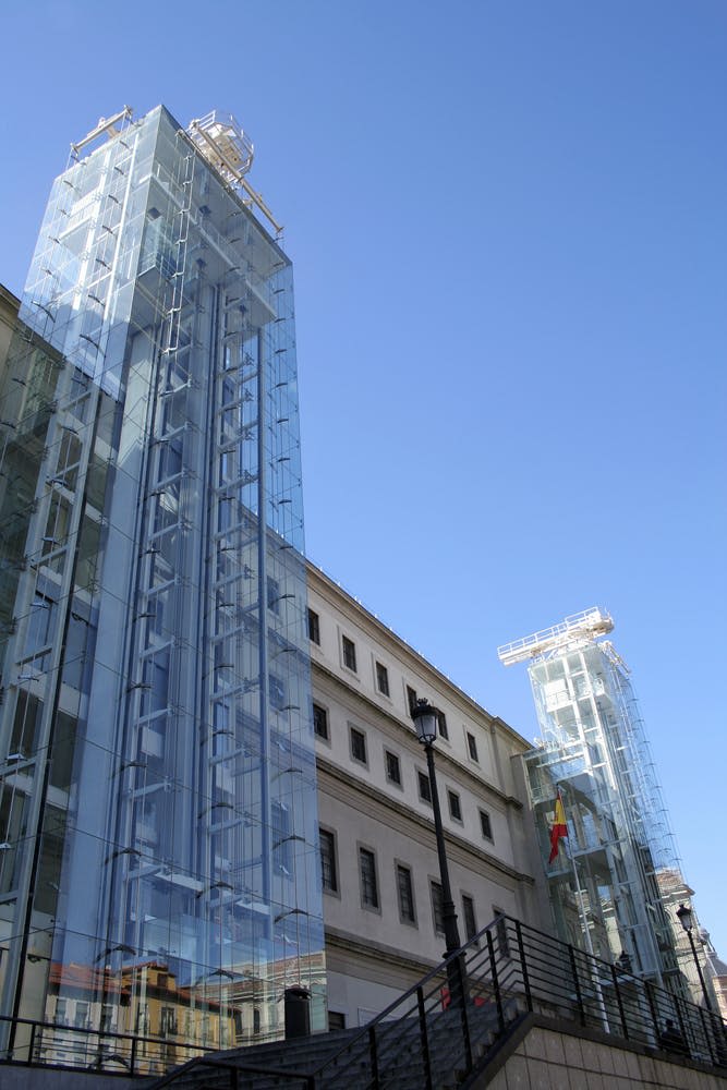 맑고 푸른 하늘 아래 여러 개의 창문이 있는 베이지색 건물에 유리 엘리베이터 타워가 붙어 있습니다.