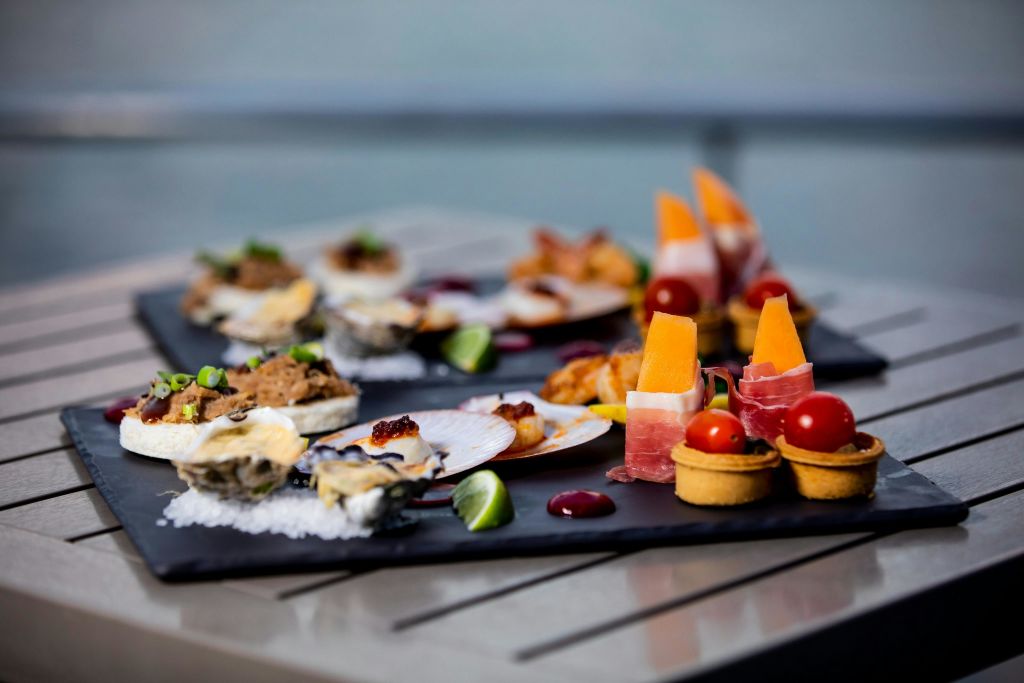 해산물, 프로슈토 포장 멜론, 한입 크기의 타르트 등 다양한 미식 애피타이저가 블랙 트레이에 정교하게 배치되어 있습니다.