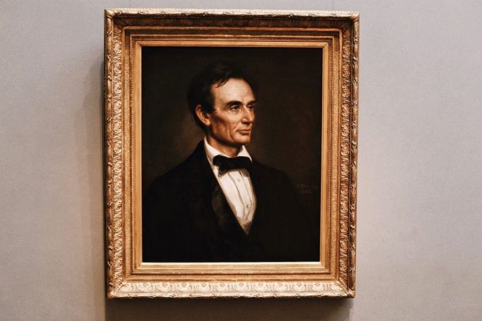 회색 벽에 검은 머리카락과 나비 넥타이를 두른 정장 차림의 남성의 액자 초상화.