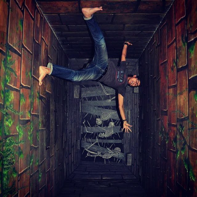 골격 생물을 배경으로 한 그림이 있는 수직 벽돌 벽에 달라붙은 것처럼 보이는 사람. 착시 효과.