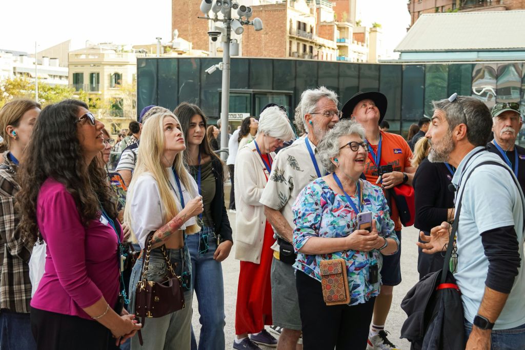 캐주얼한 복장을 한 사람들이 도시 야외에서 위를 바라보며 서 있습니다. 건물이 배경으로 보입니다.