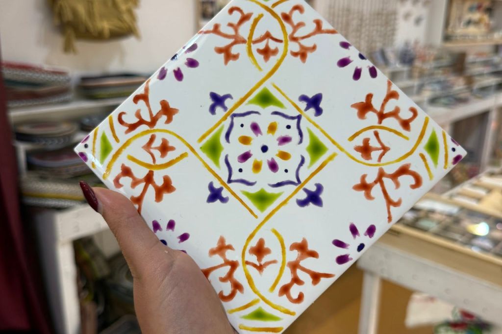 다채로운 꽃무늬와 기하학적 무늬가 있는 장식용 세라믹 타일로, 못을 칠한 사람이 들고 있습니다.